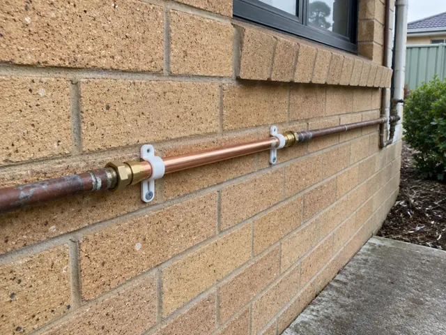 Repaired copper water pipe fixed to a brick exterior wall with clips in Greystanes