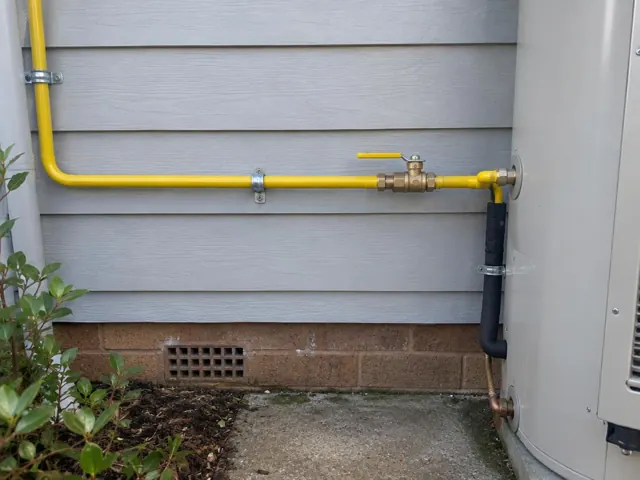 Yellow gas pipe and valve mounted on an exterior wall beside a home unit in Abbotsbury